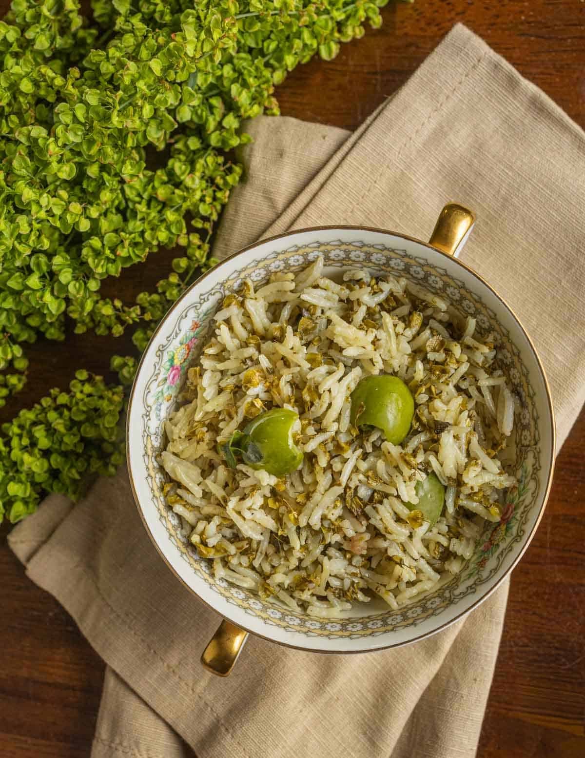 Unripe green dock seeds cooked with rice and green olives with green dock seeds on the plant on the side.