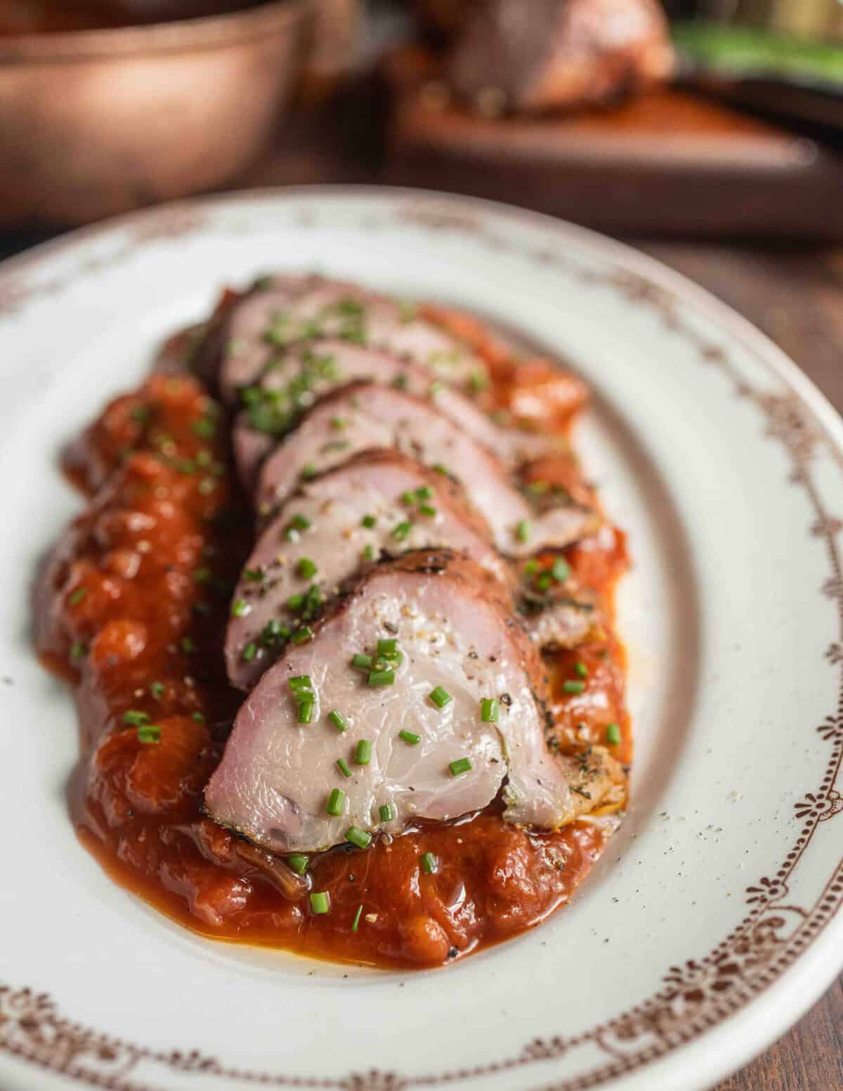 Smoked pork roast sliced on a plate on a bed of savory rhubarb sauce.