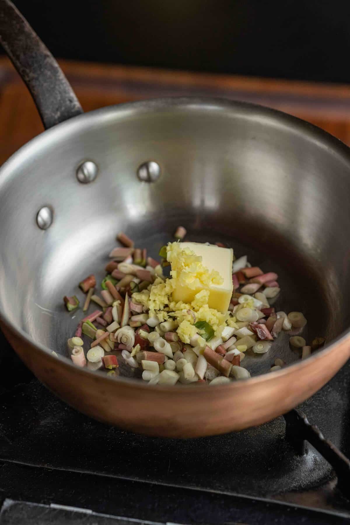 Cooking sliced garlic and shallot or ramps in butter in a saucepan.