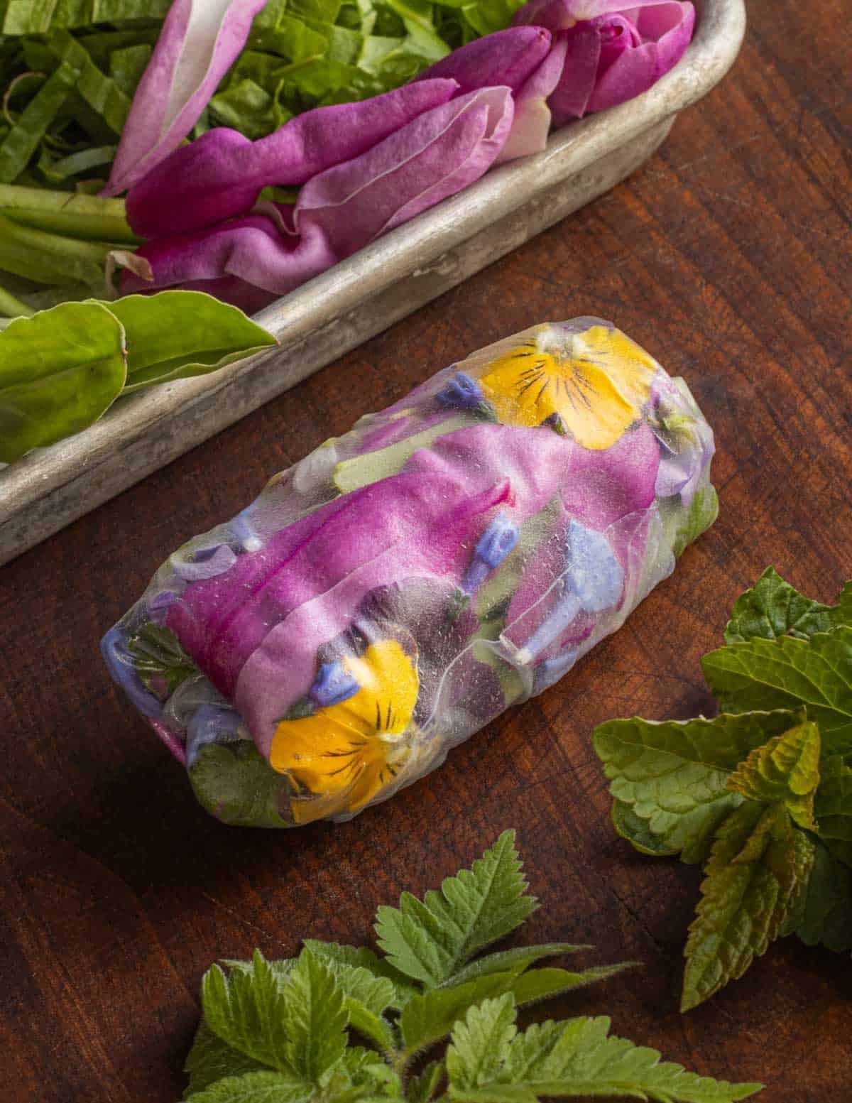 A close up image of spring rolls next to a tray of garnishes and fresh greens. 