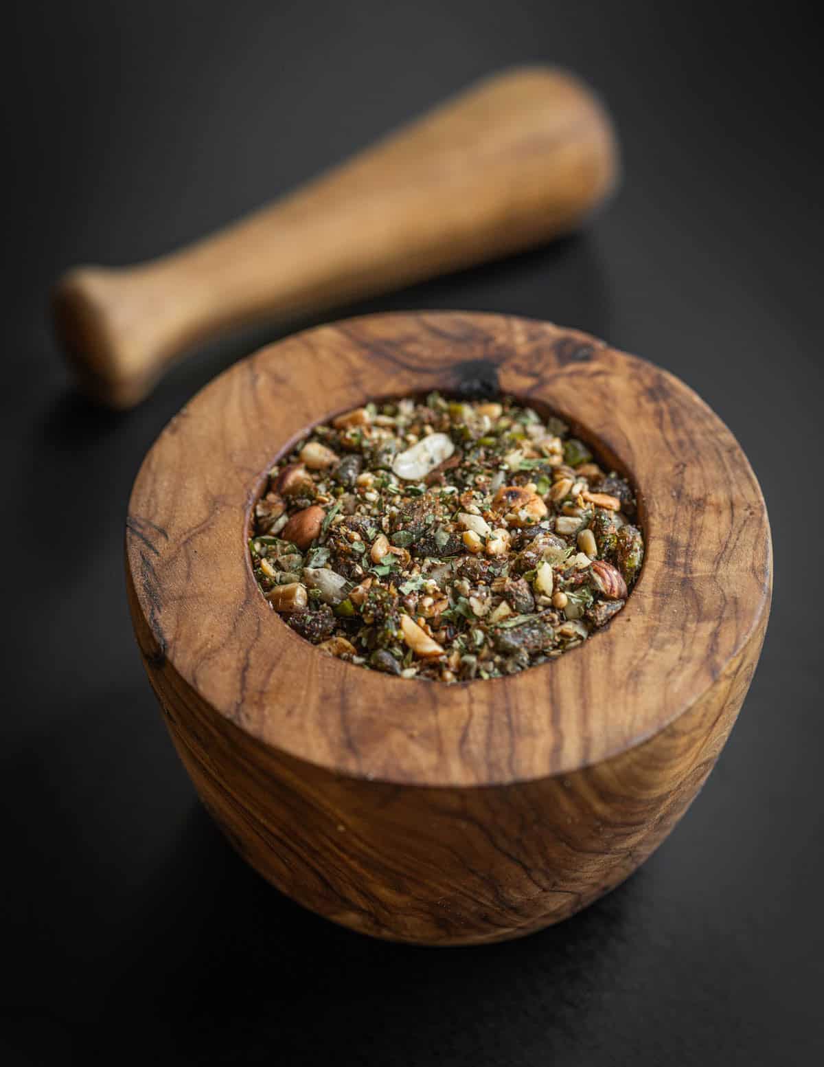 Dukkah spice mixture made with wild nuts and maple seeds shown in a wooden mortar and pestle.