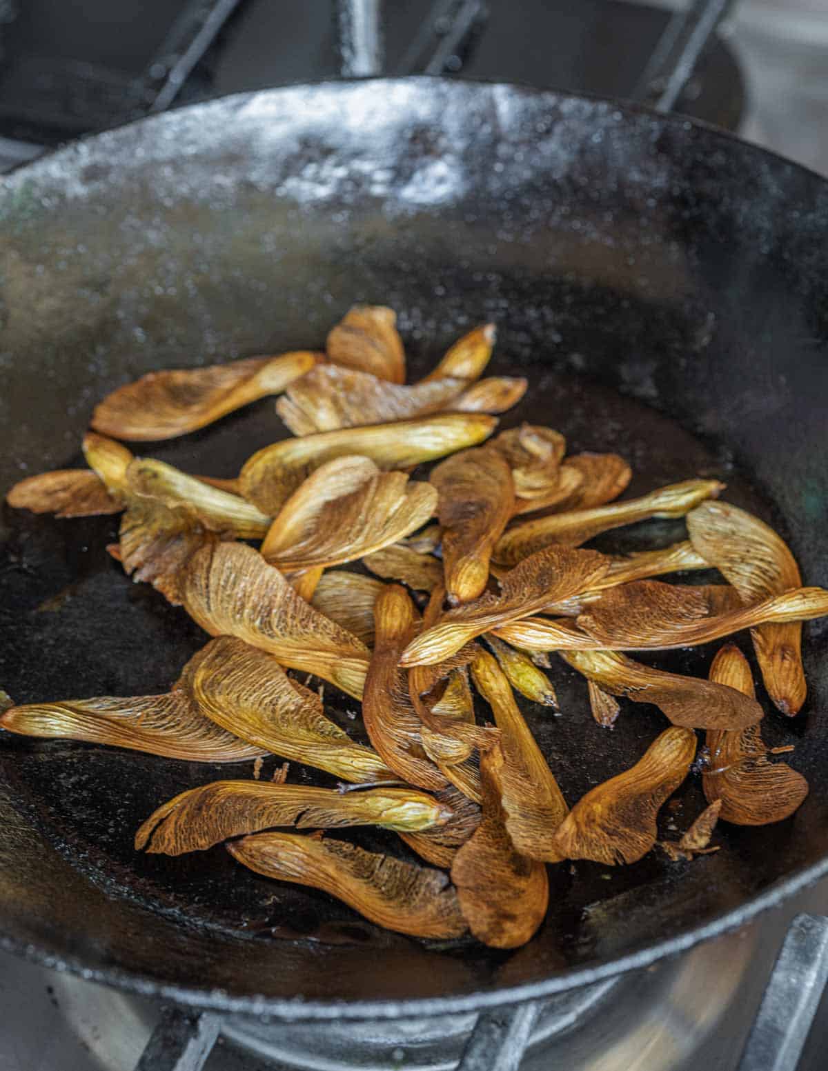 A black carbon steel pan filled with roasted maple samaras.