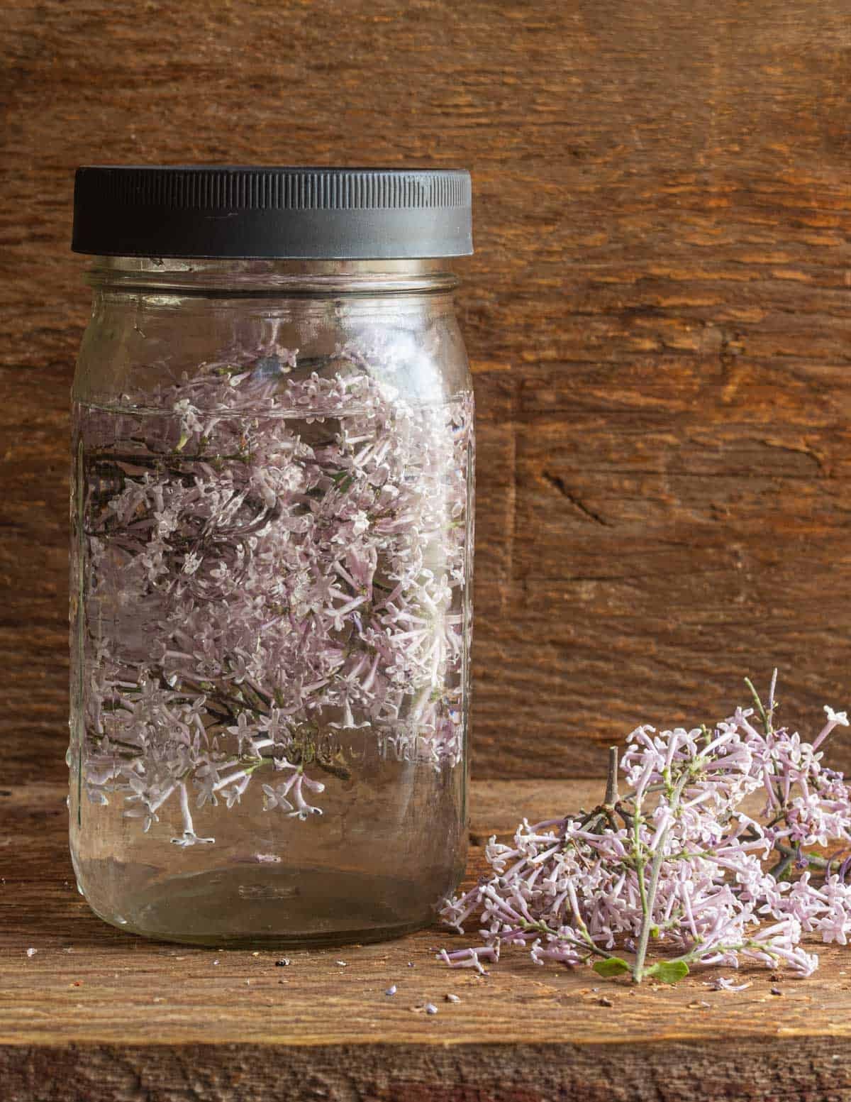 A jar of water infusing with fresh lilac sprigs.