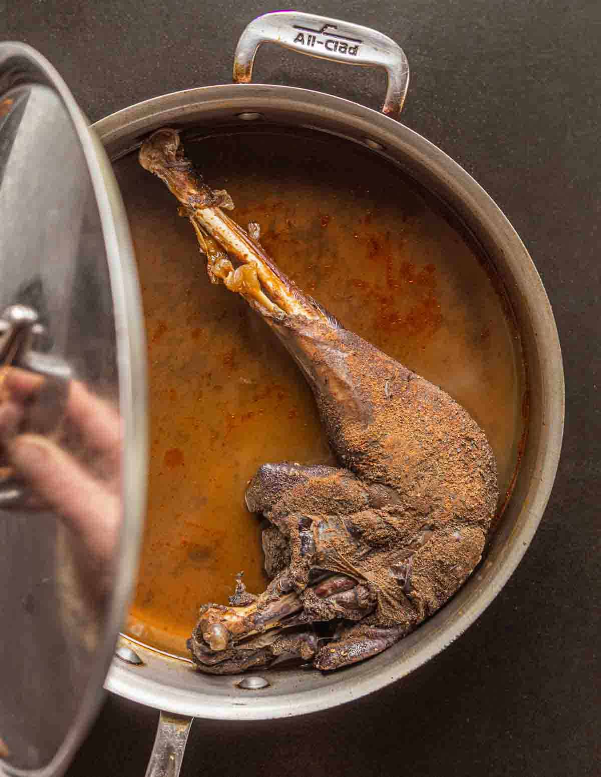 A cooked wild turkey leg in a pan with liquid on a black background.