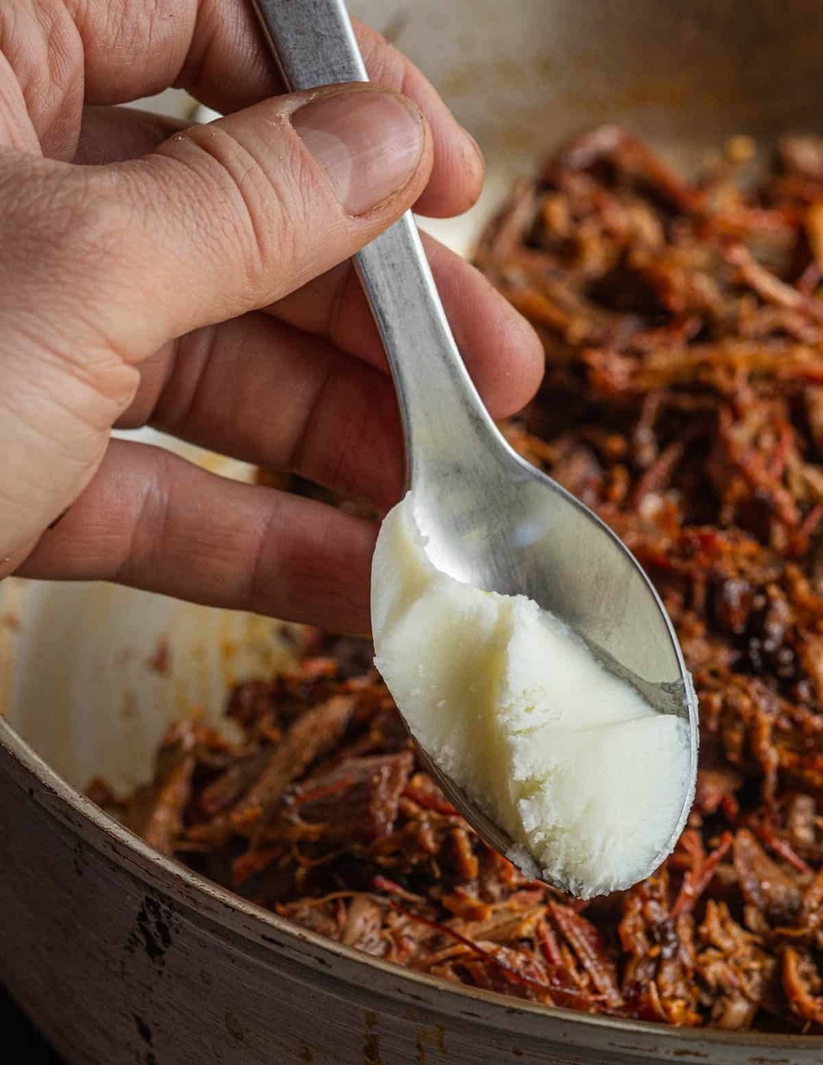 Adding duck fat to a pan of cooked, pulled wild turkey meat.