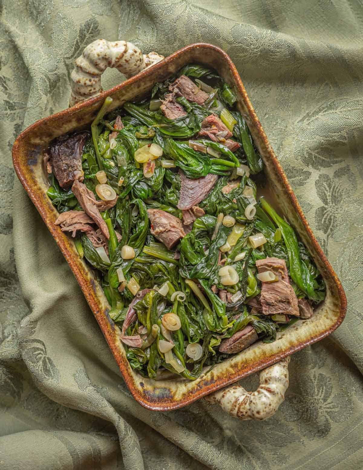 Diced smoked turkey leg meat with wild greens in a ceramic dish seen from above.