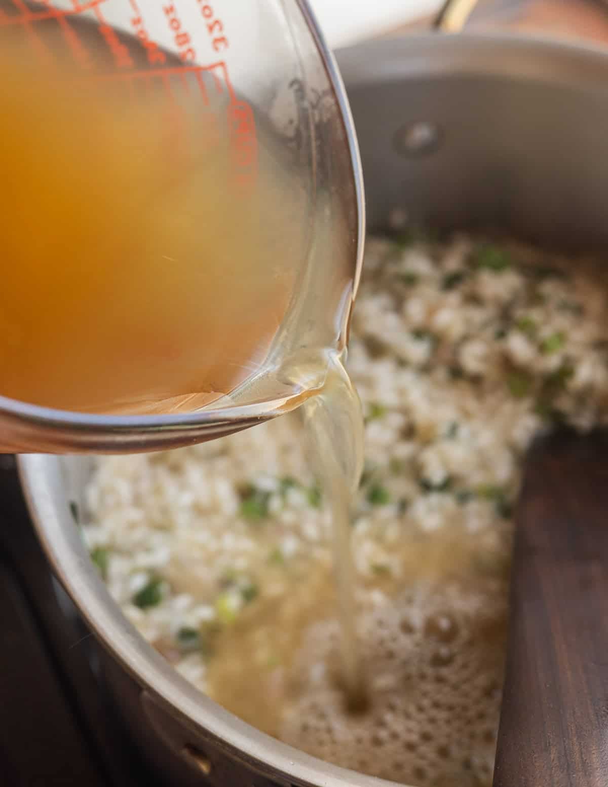 Adding chicken stock to a pan of risotto rice cooking with ramps.