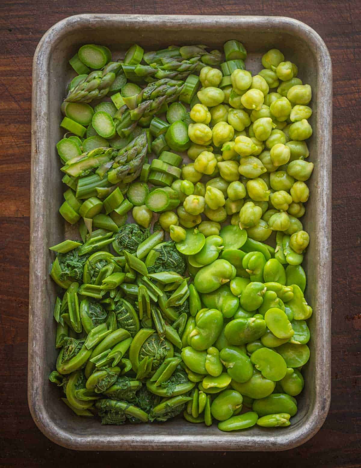 Asparagus, green chickpeas, fava beans and fiddlehead ferns on a tray.