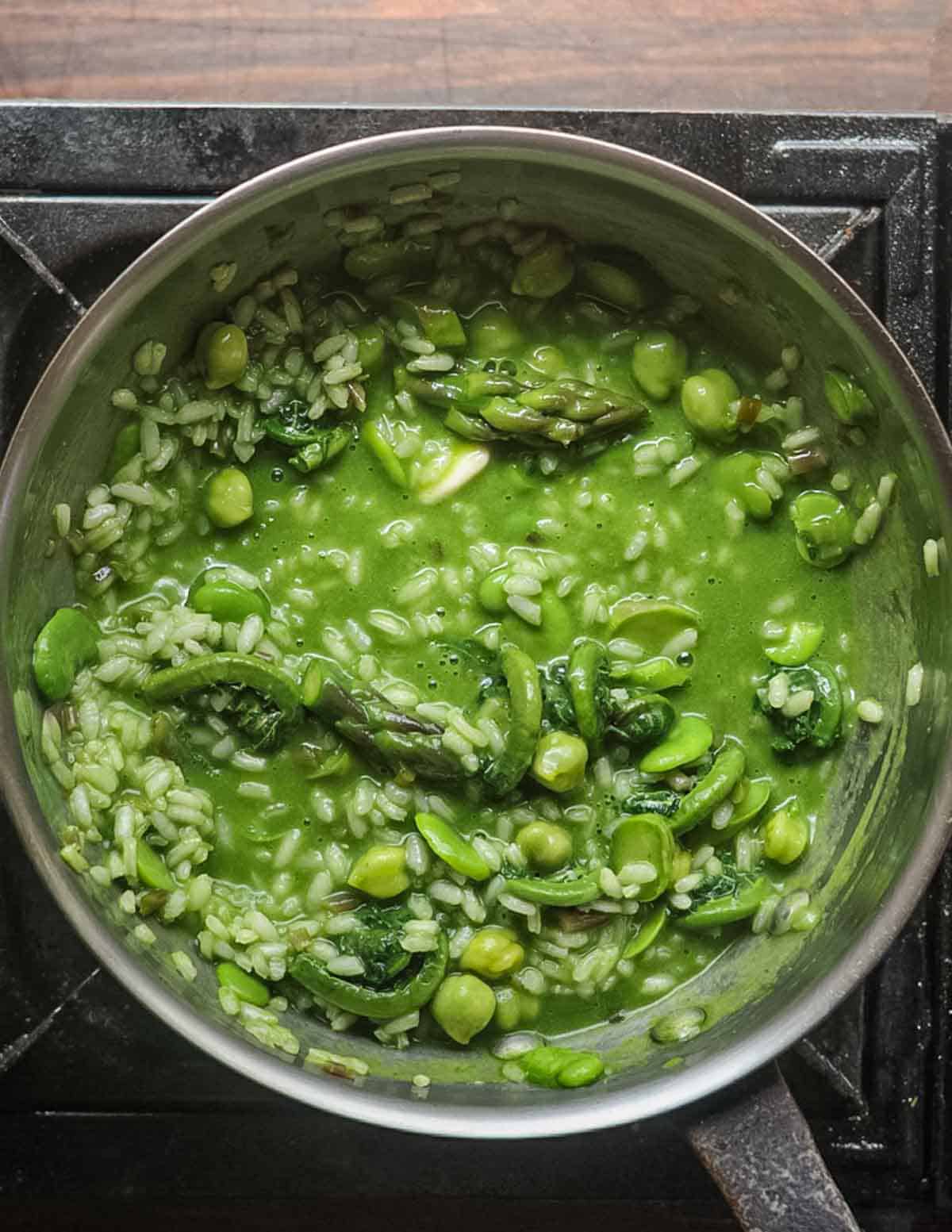 A pan of green risotto showing butter being stirred into finish.