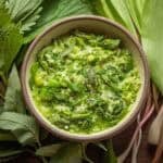 A bowl of very green spring risotto verde made with fiddleheads, asparagus, fava beans, and chives. Fresh ramps and a nettles are shown on the side.