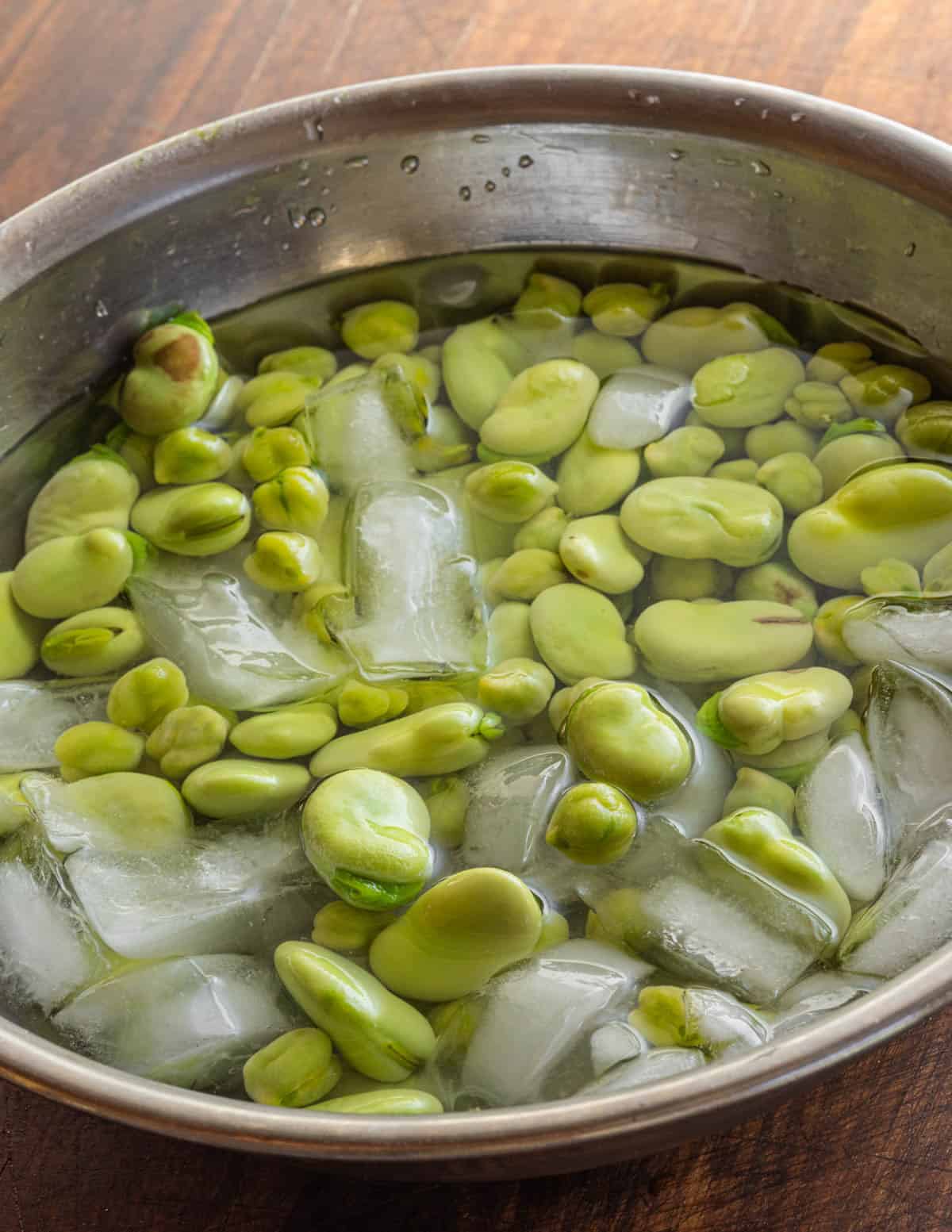 Chilling blanched green chickpeas and fava beans in a bowl of ice water.
