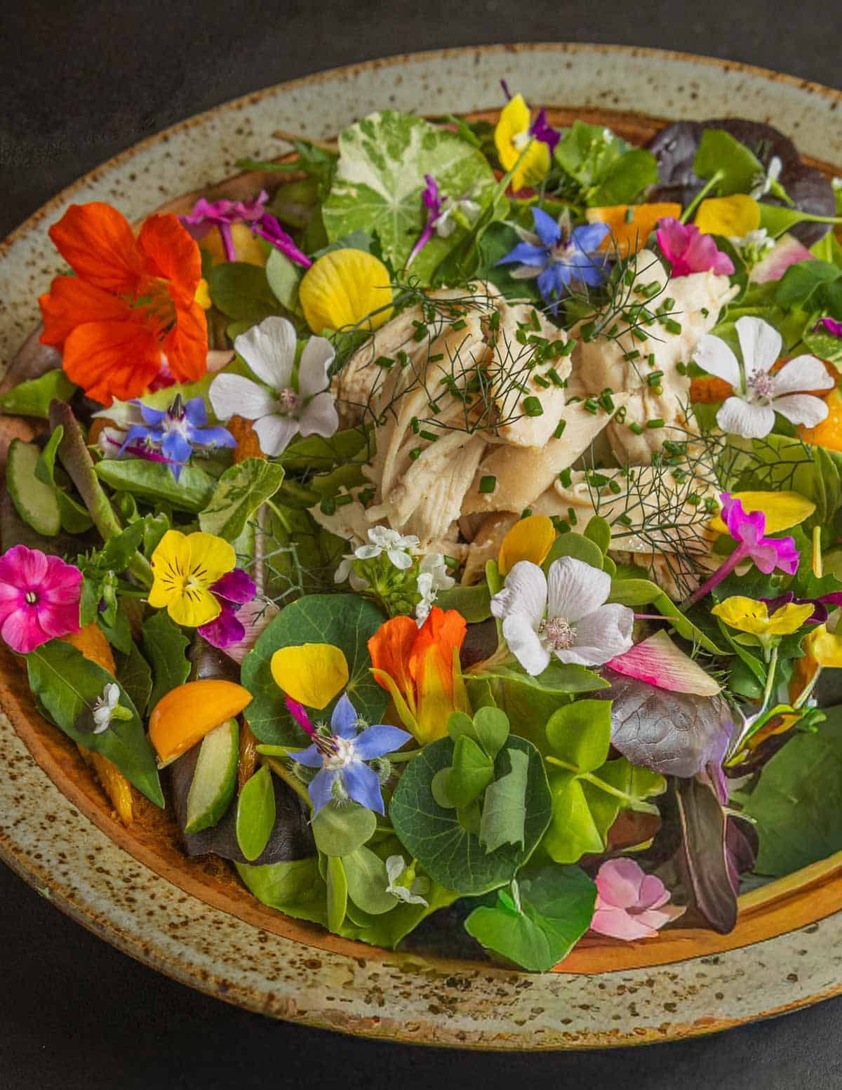 A close up image of a salad with roast chicken and many edible flowers including begonias.