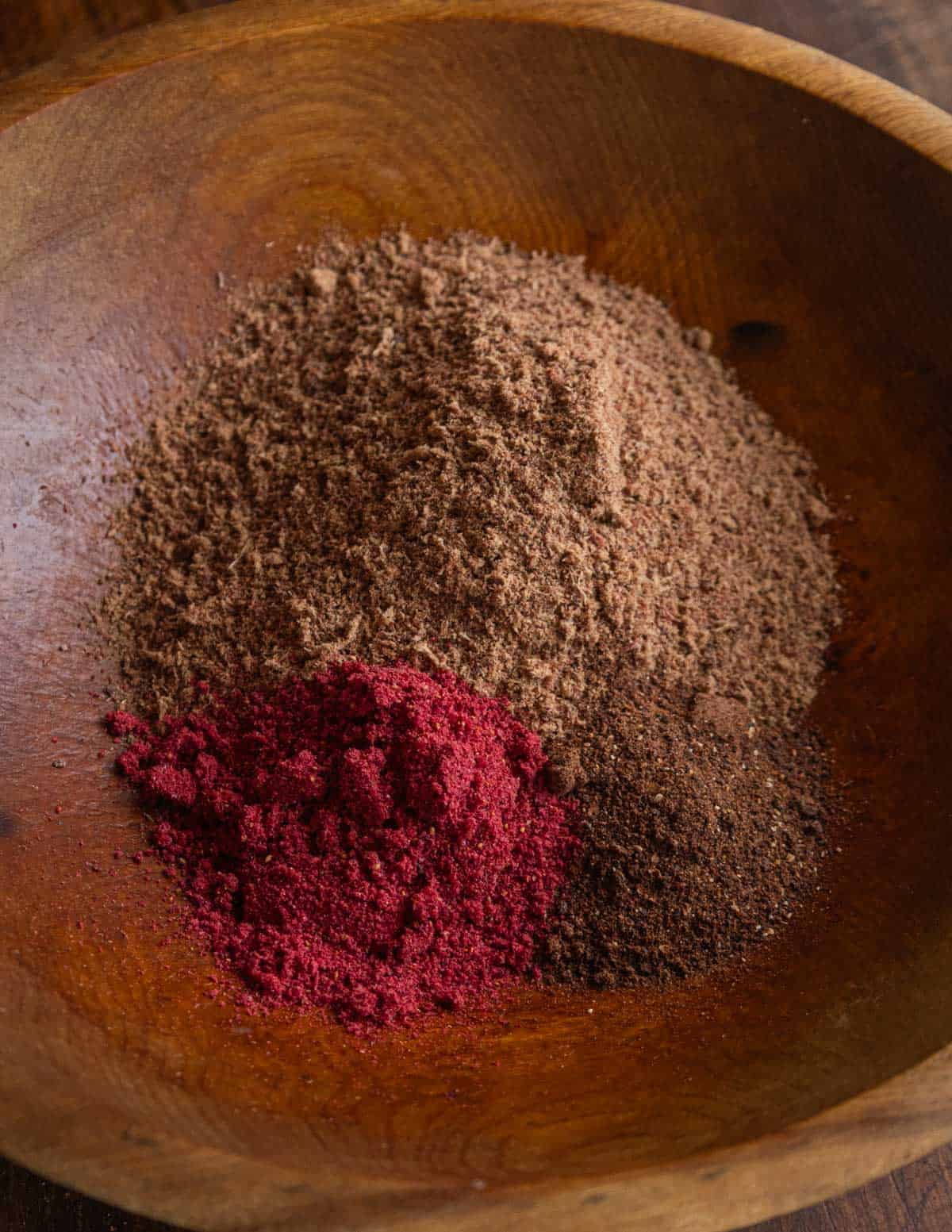 A wooden bowl where dried ground venison is being mixed with dried cranberry and serviceberry powder.