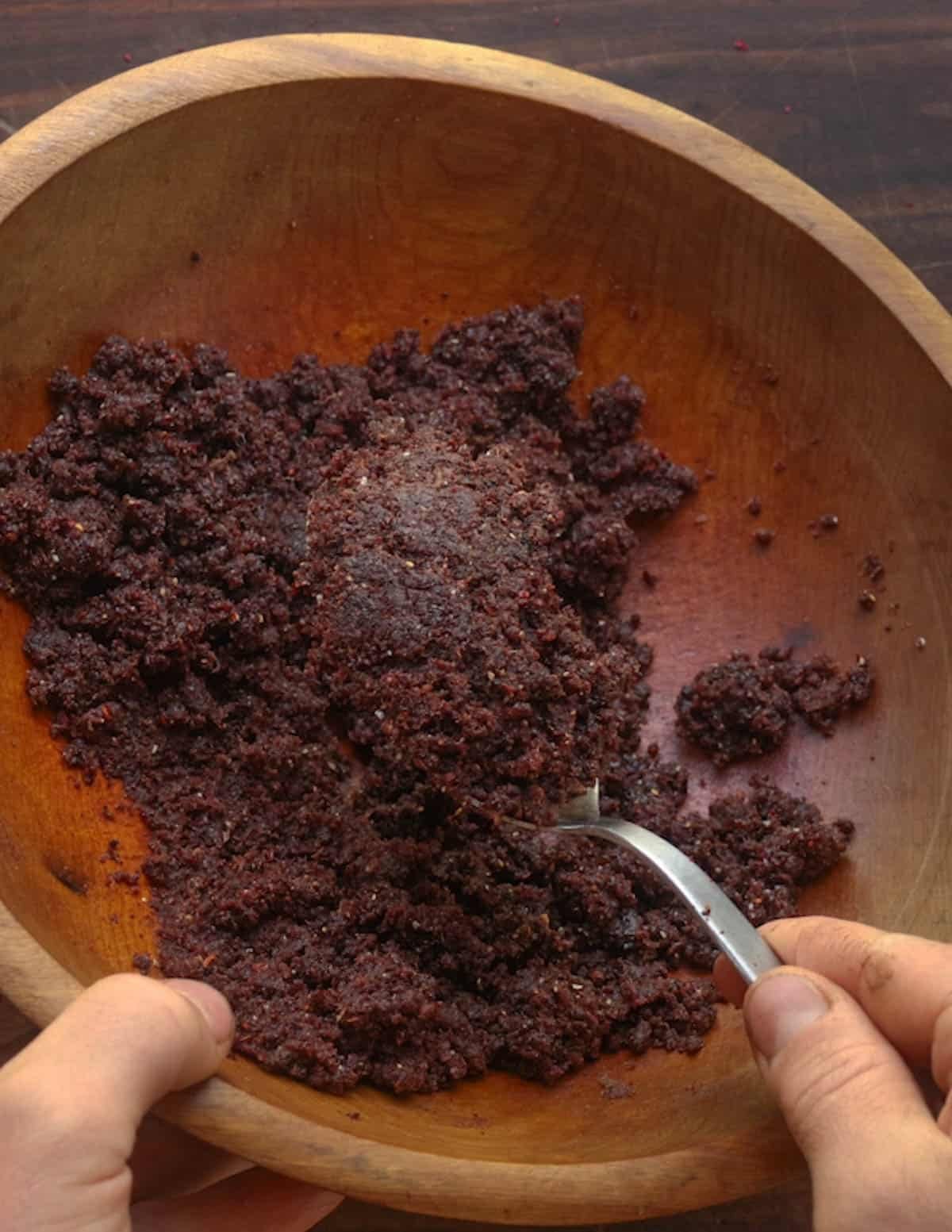 Stirring the ground meat, fruit, tallow and maple until it comes together in a mass.