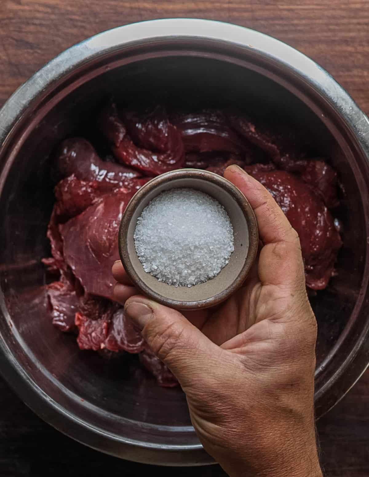 Adding kosher salt to trimmed venison in a bowl for making pemmican.