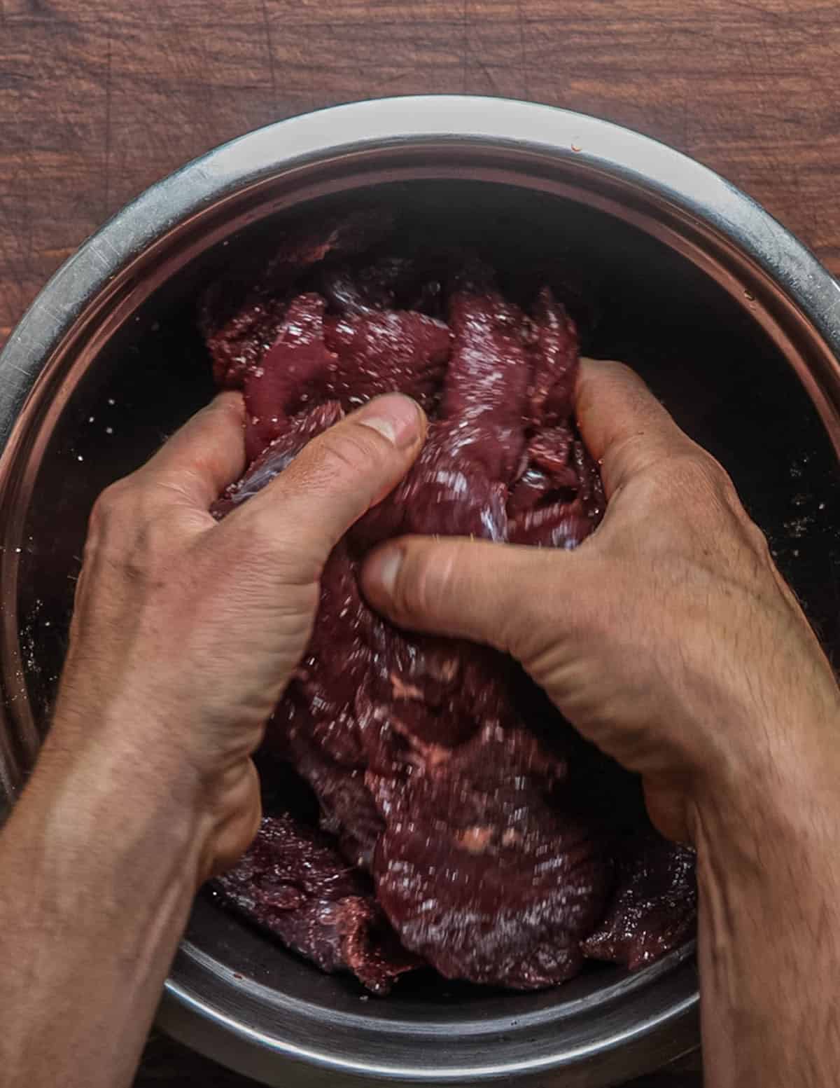 Mixing venison with salt in a large bowl before refrigerating overnight to make pemmican.