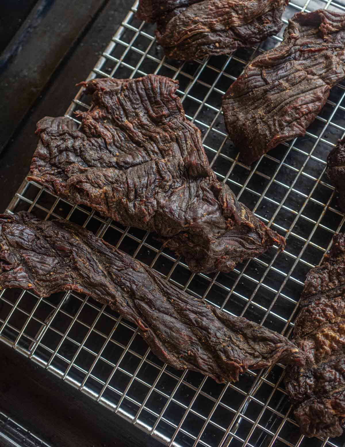 Strips of finished smoked, dried venison laying on a drying rack.