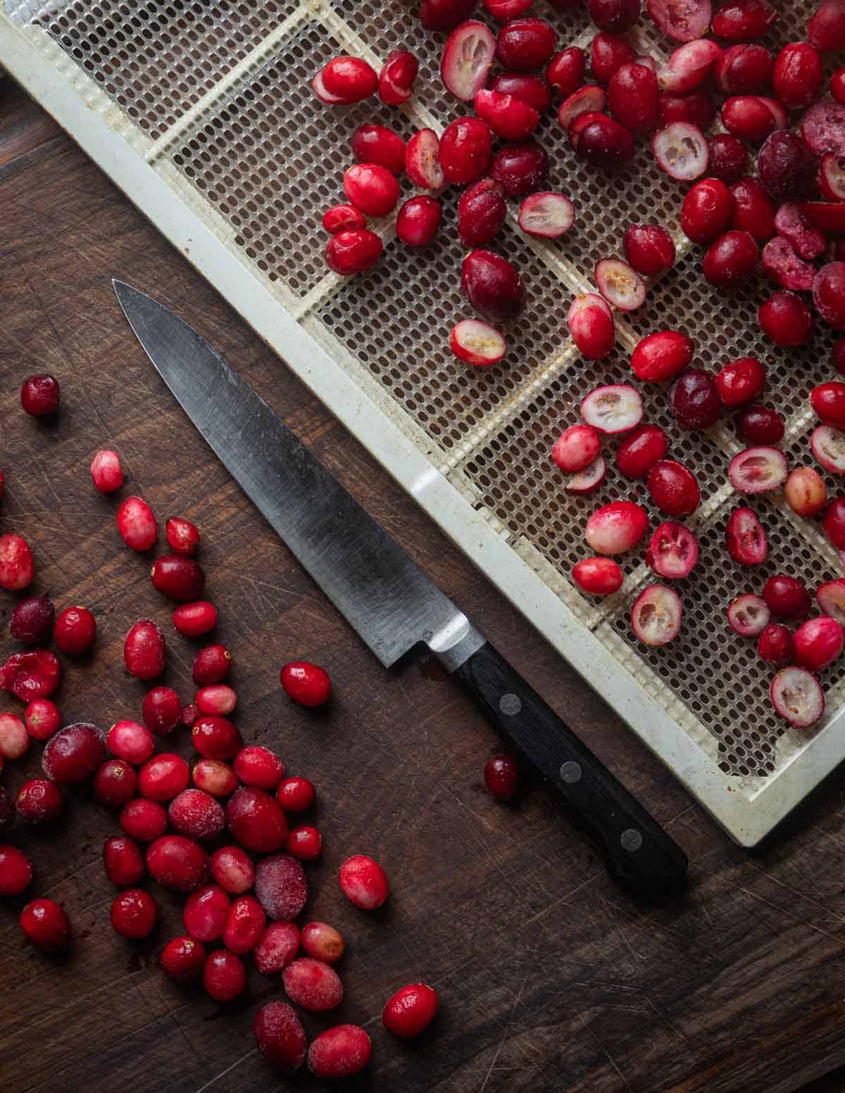 Cutting fresh cranberries in half with a paring knife and putting them on a dehydrator.