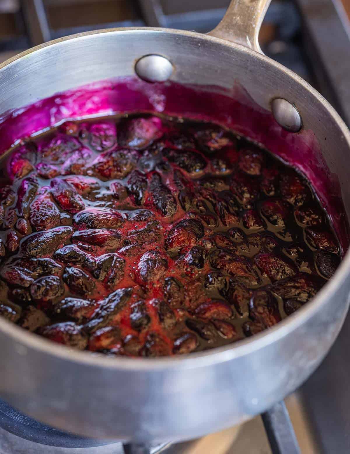 Honeyberries being cooked in a pan showing a bright purple color from cooking the fruit.