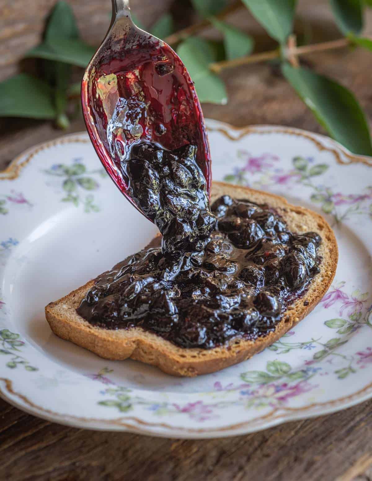 A spoon pouring freshly cooked honeyberry or haskap berry jam on a piece of buttered toast.