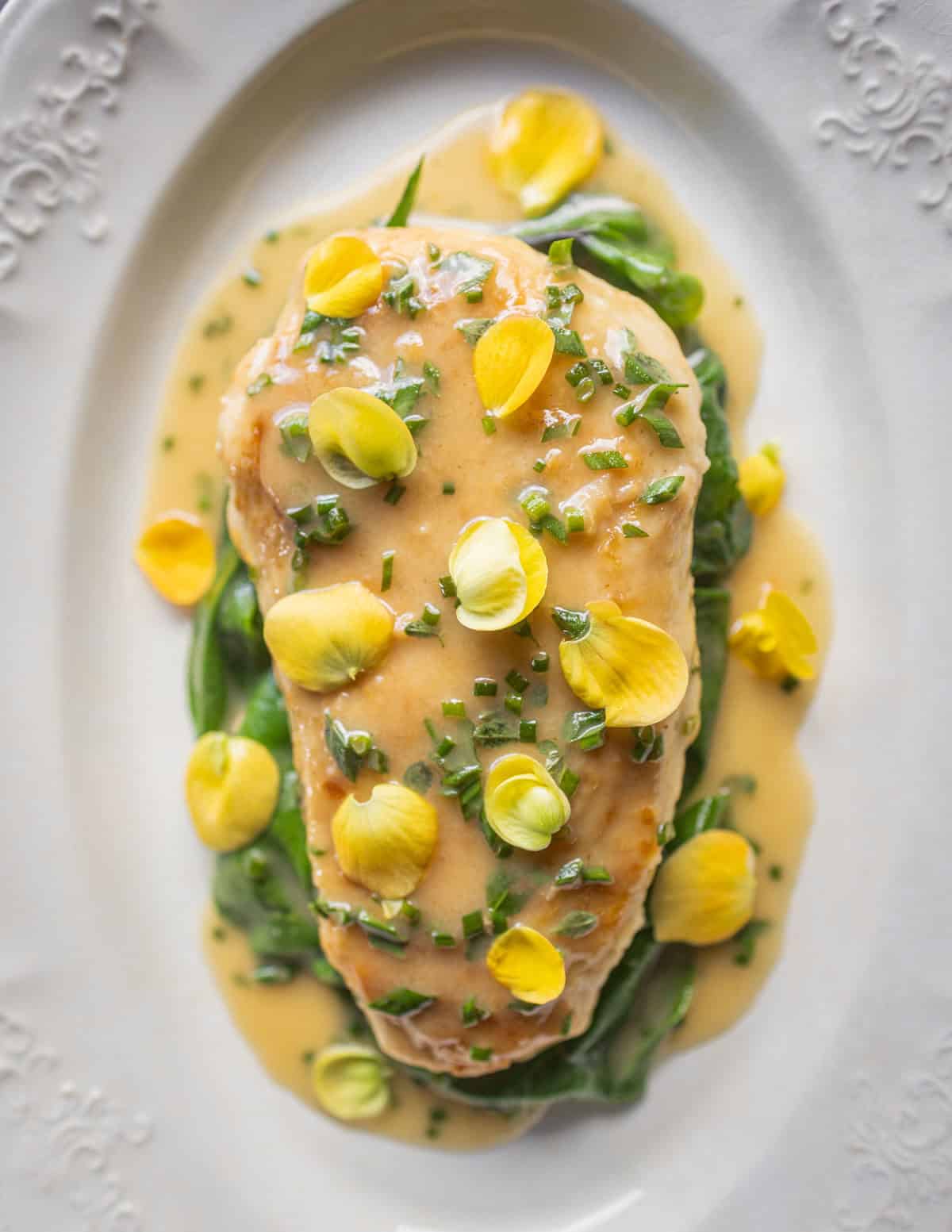 Chicken in lemon sauce with herbs and lemongrass garnished with yellow tuberous begonia flowers.