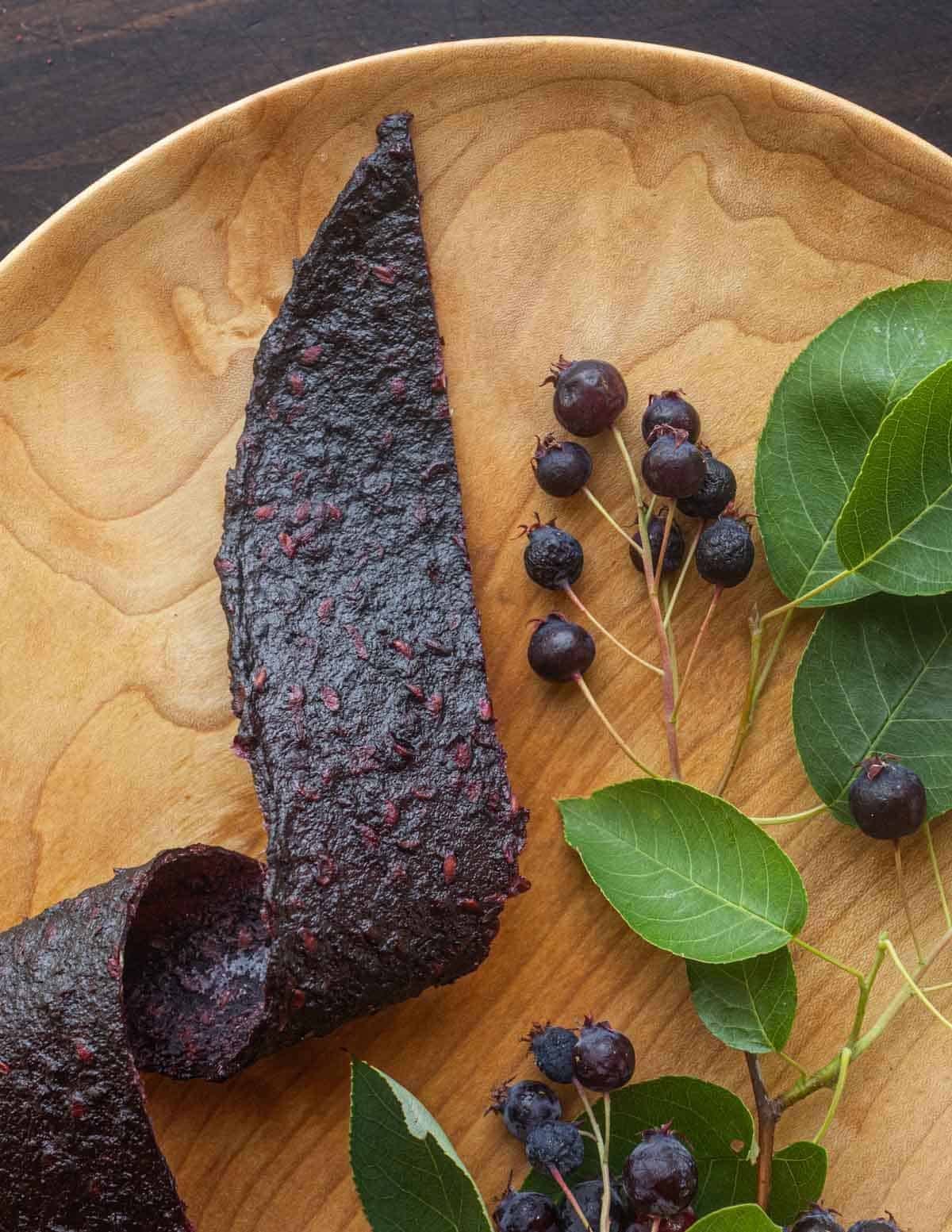 Dried serviceberry or juneberry leather next to a serviceberry branch on a birch wood plate.