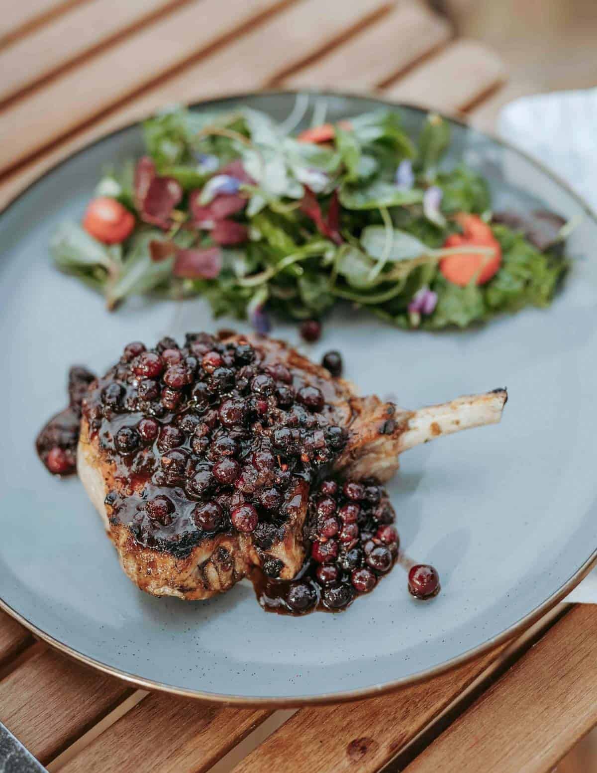 A pork chop with juneberry sauce next to a salad on a blue plate made for camping.