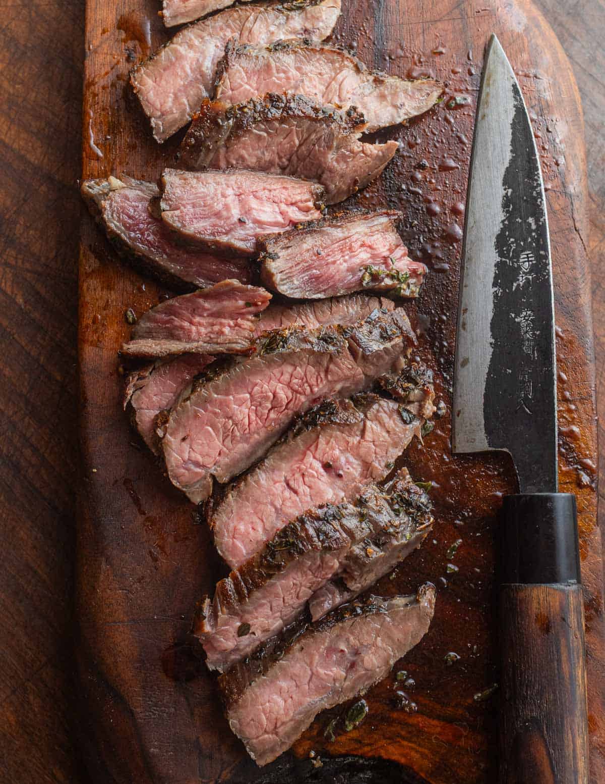 Sliced flank steak cooked medium rare and sliced on a cutting board next to a Japanese knife.