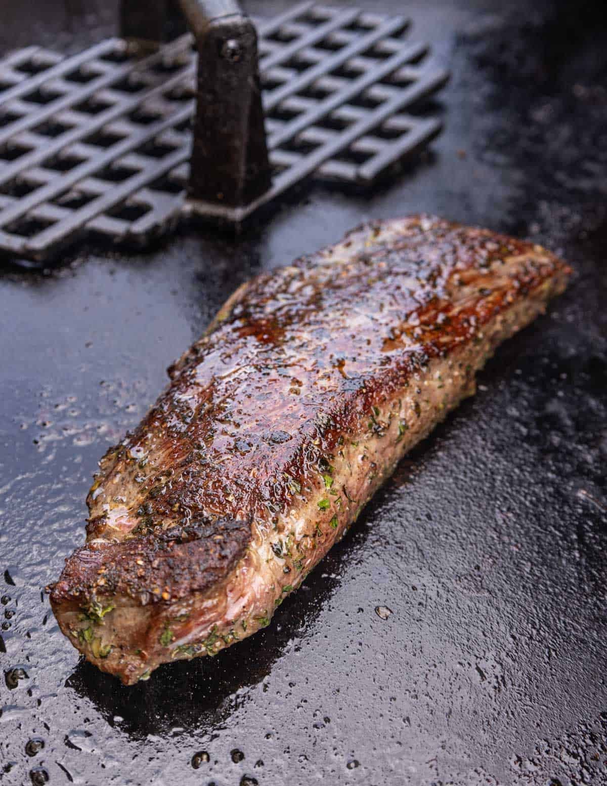 Golden brown flank steak cooking on a blackstone flattop griddle.