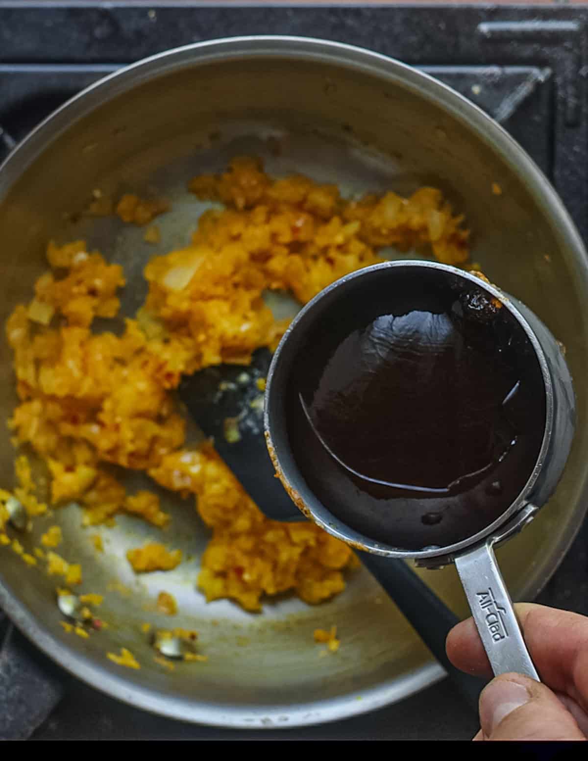 Adding meat stock to a pan of aromatics cooking in palm oil.