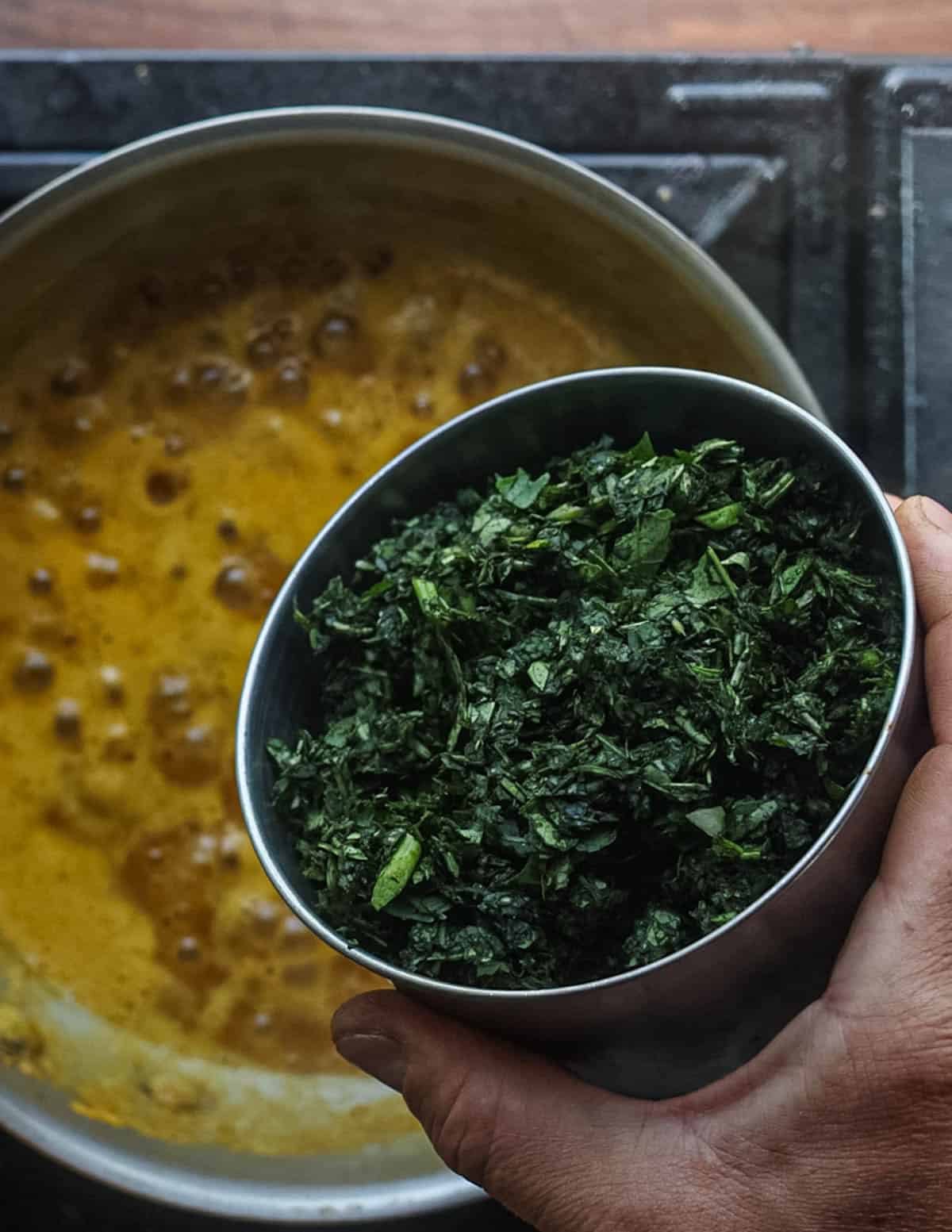 Adding finely chopped sweet potato greens to a pan of stock and aromatics.