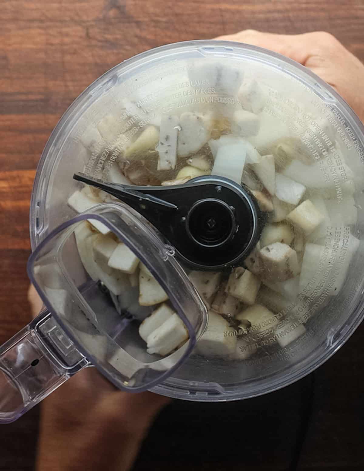 A food processor filled with ginger, garlic, shallot, leek, onion and eggplant.