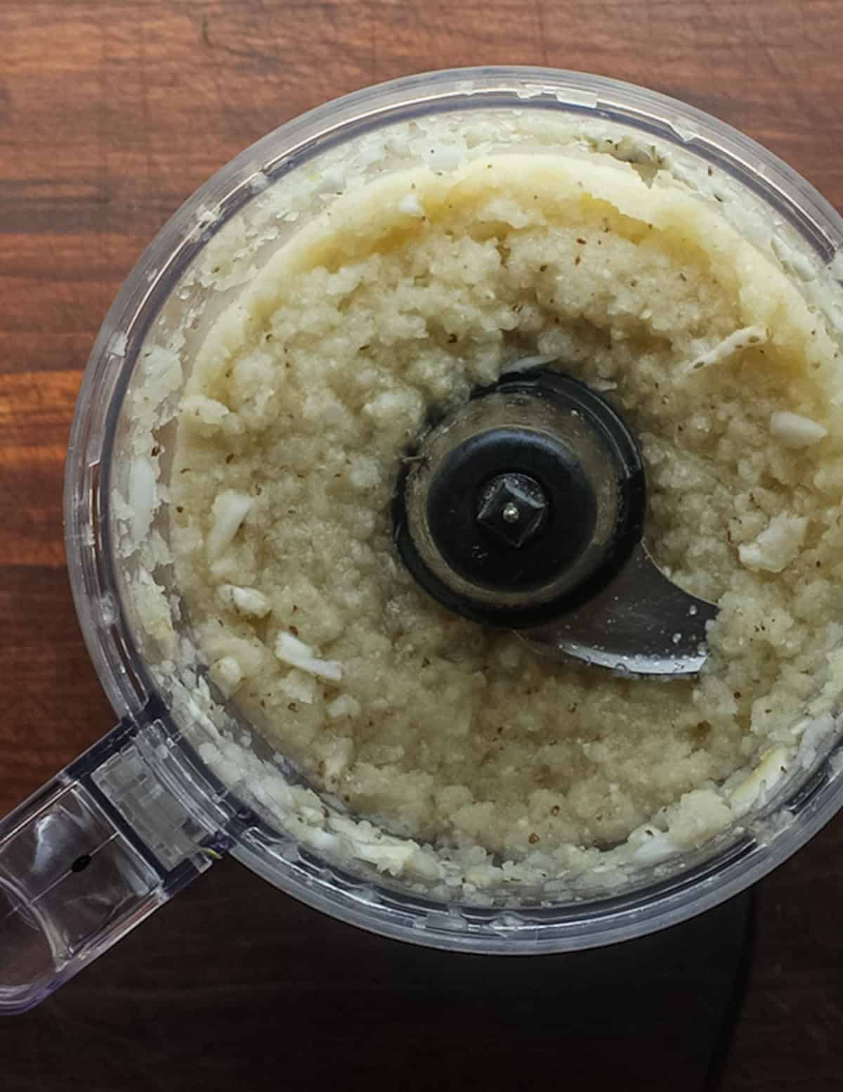 A food processor filled with pureed aromatic vegetables for sweet potato greens stew.