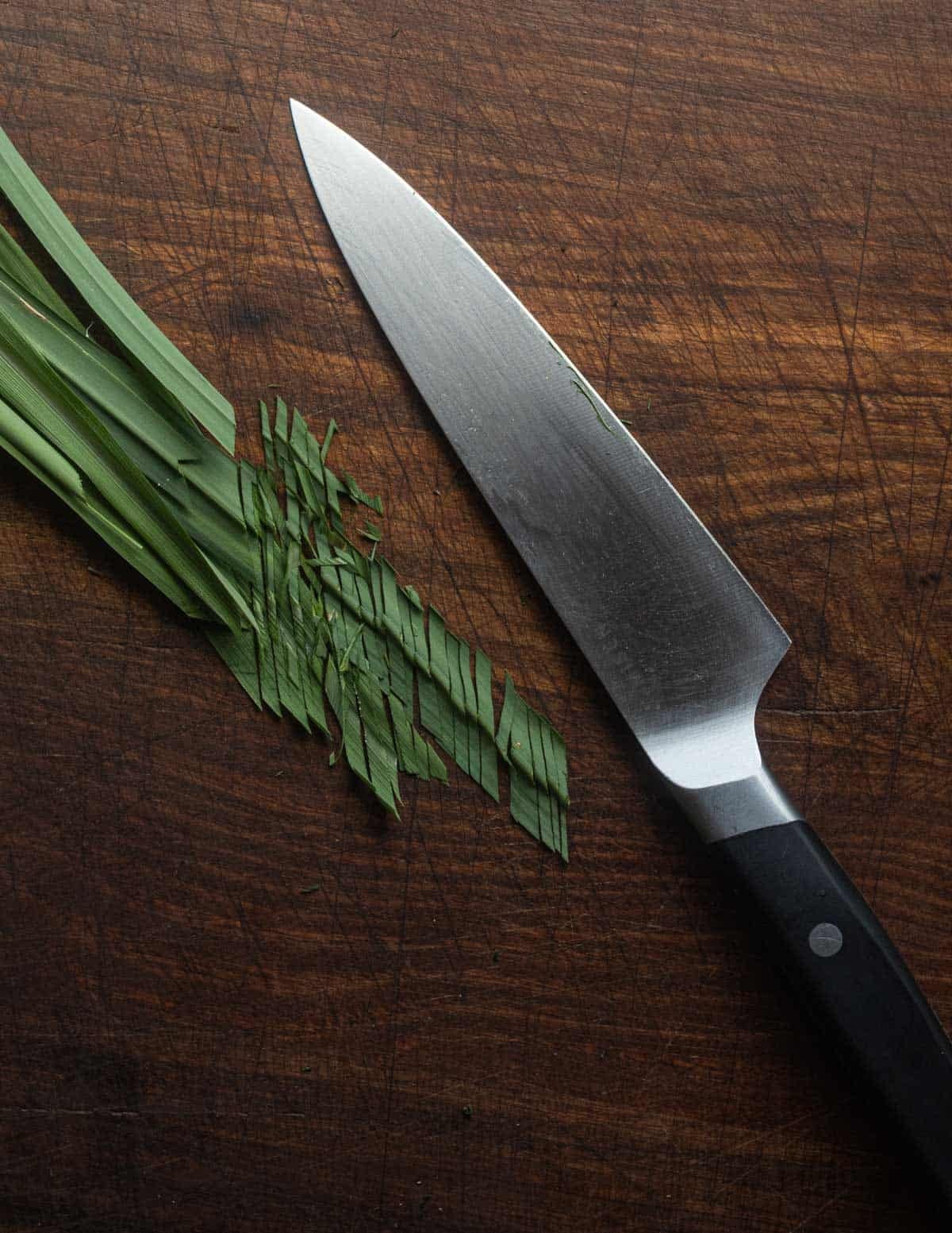 A knife finely chopping blades of fresh lemon grass.