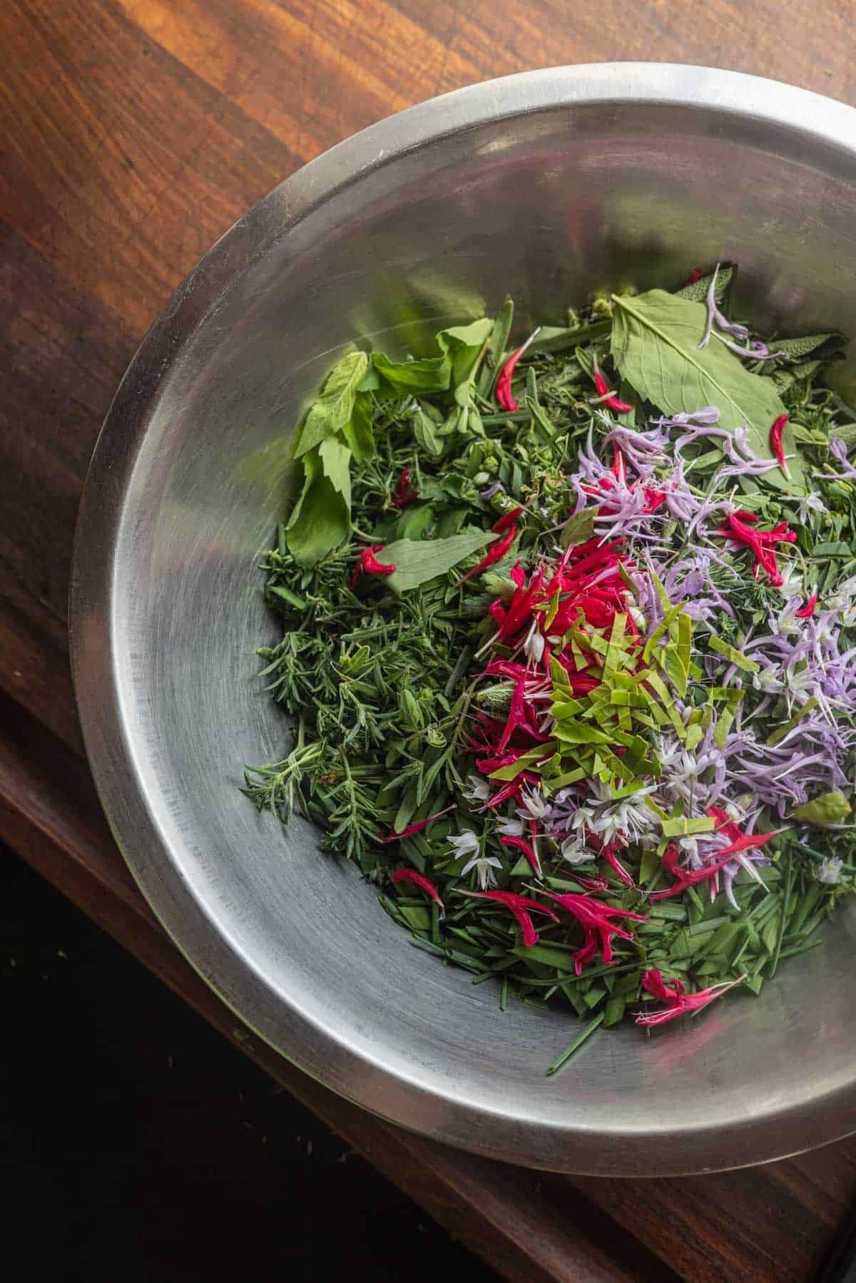 A bowl filled with fresh garden herbs and aromatic bee balm flowers.