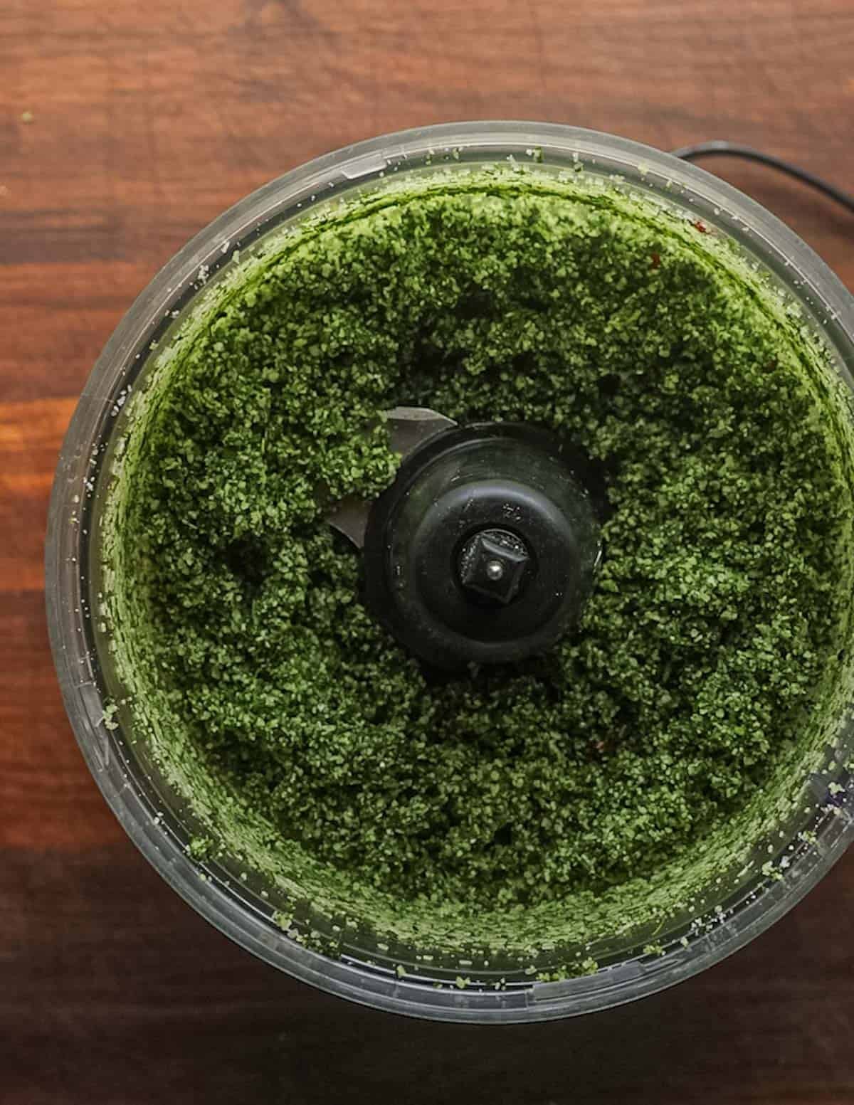 A food processor filled with pureed green herb salt.