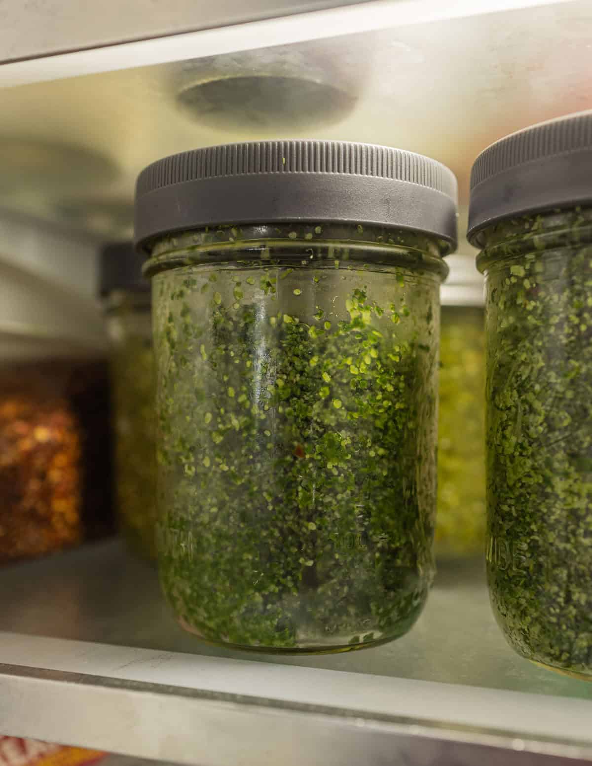 Jars of green herb salt in a refrigerator.