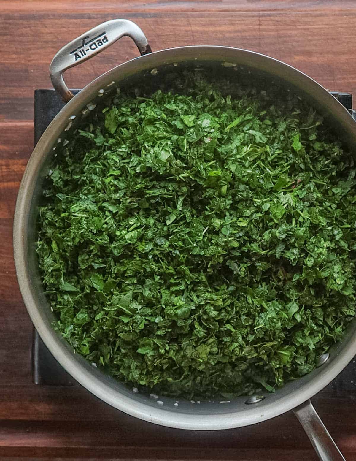 A wide All Clad pan filled with finely chopped foraged greens.