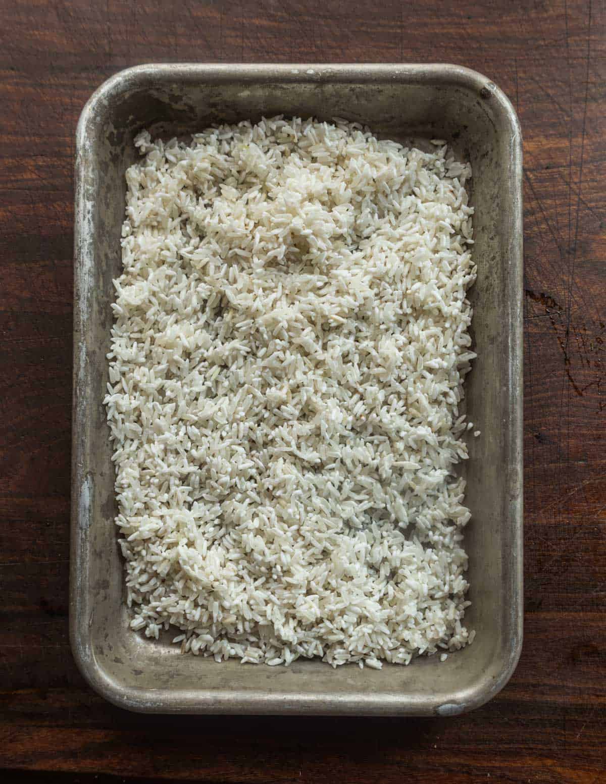 A small baking sheet filled with rice that's been dried after rinsing.