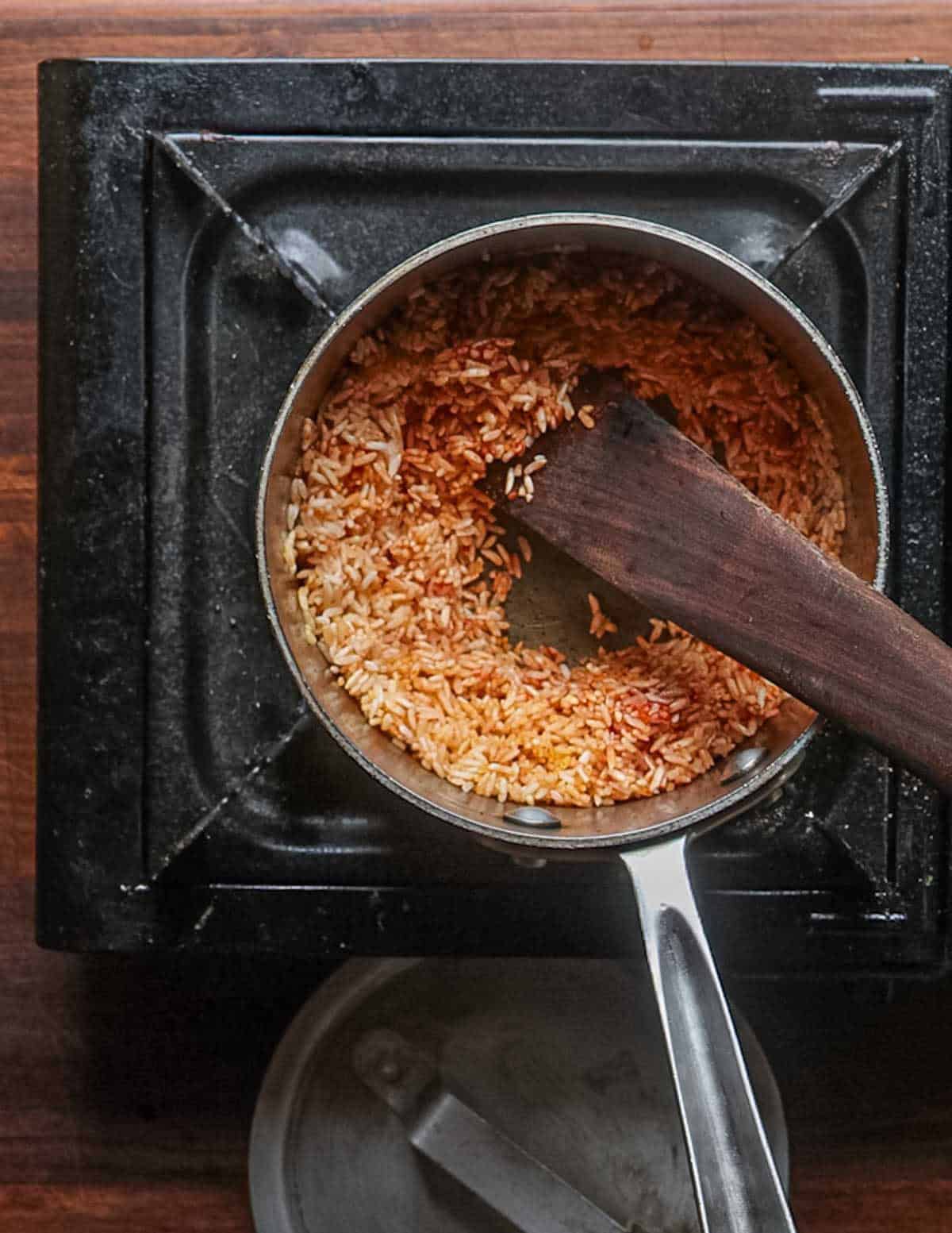 Stirring cooking rice in a pot with tomato paste before adding water.
