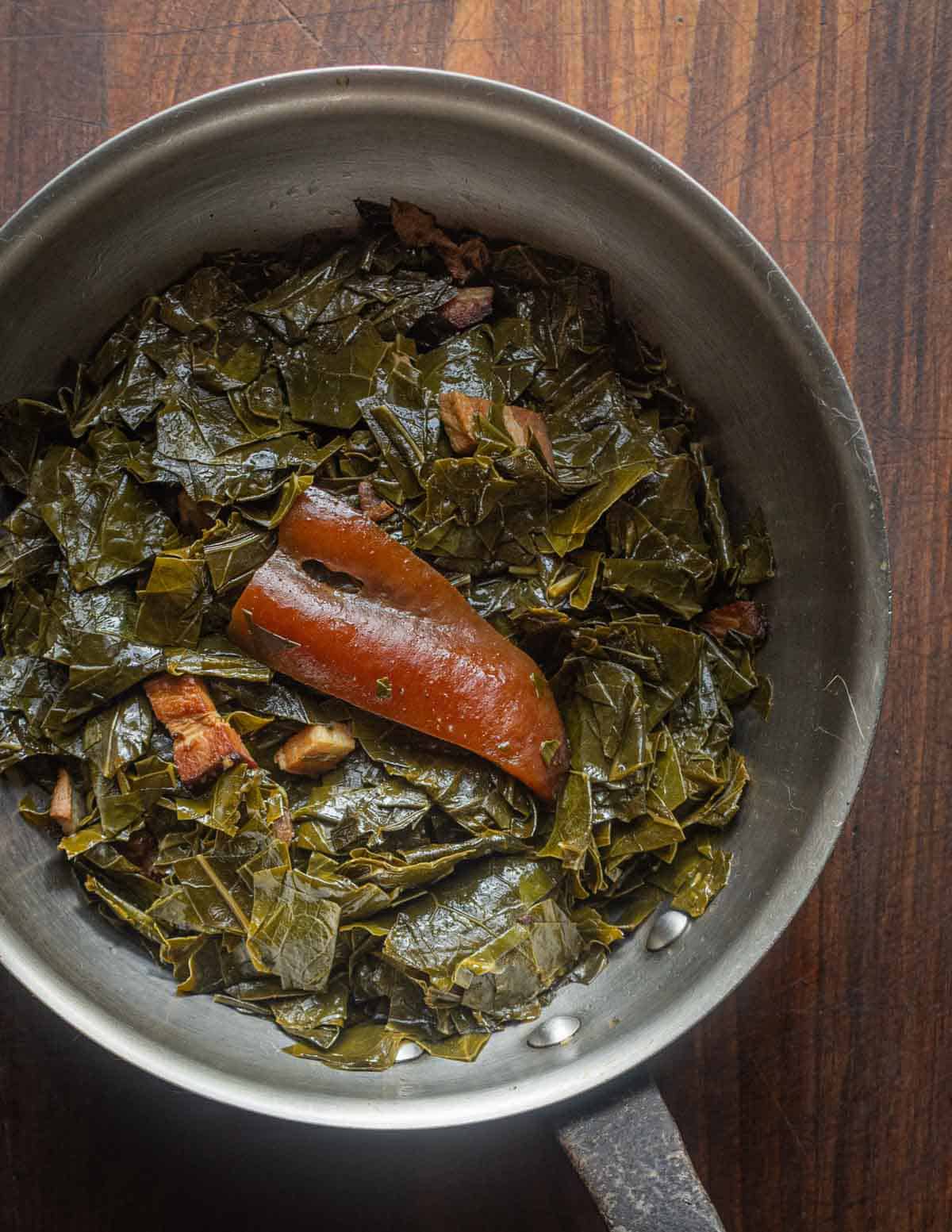 Braised kohlrabi greens cooked like collard greens with bacon and a piece of bacon rind in an old copper pan.