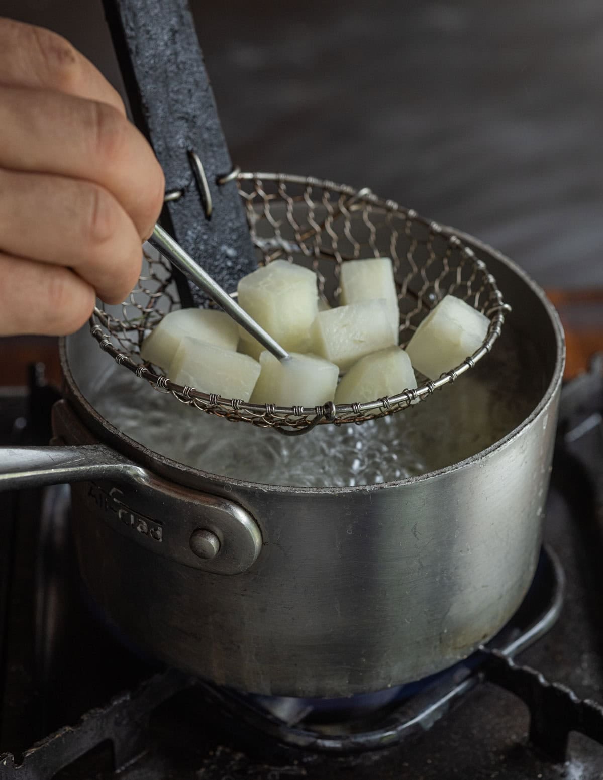 Testing the doneness of kohlrabi in a pot of boiling water by poking it with a sharp skewer.