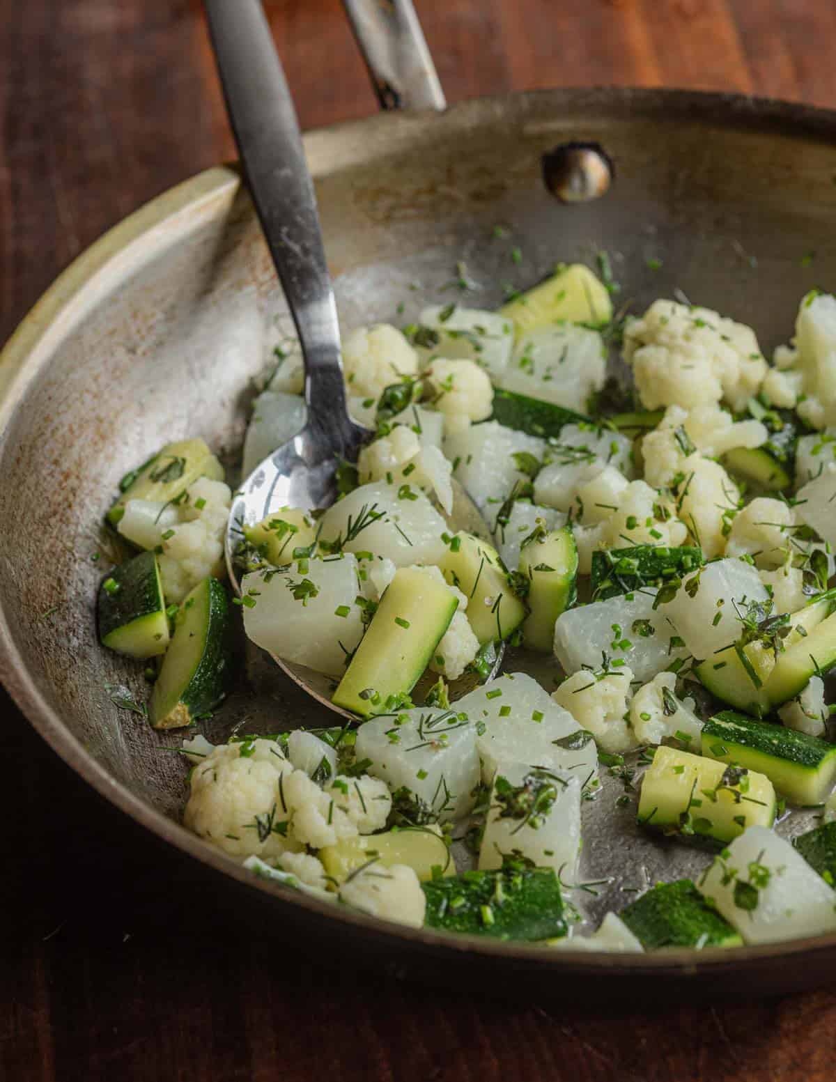 A pan of diced kohlrabi, cauliflower, and zucchini with herbs, chicken stock and butter.