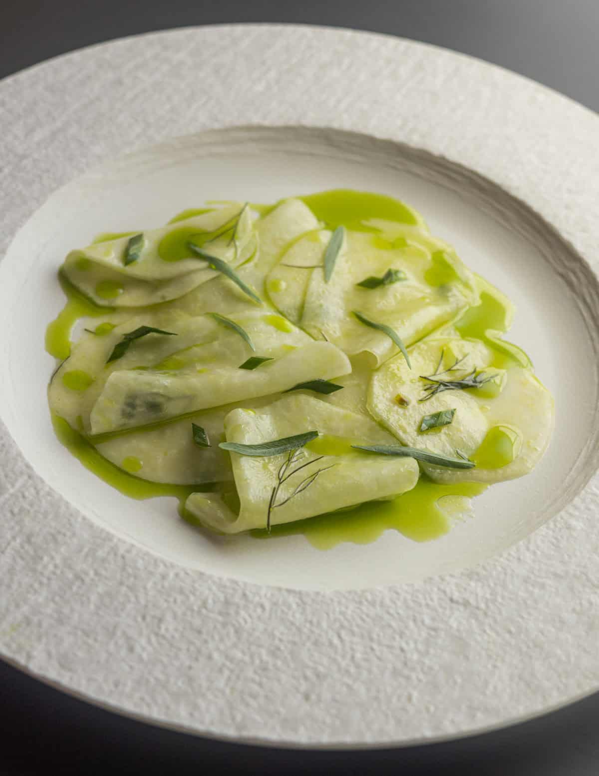 A plate of shaved kohlrabi with herbed walnut oil, bronze fennel, tarragon and lemon on a white china plate.