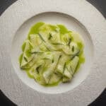 Kohlrabi salad with green herb oil, fresh herbs and lemon on a white china plate.