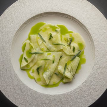 Kohlrabi salad with green herb oil, fresh herbs and lemon on a white china plate.