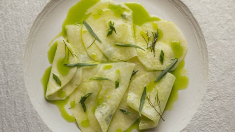 Kohlrabi salad with green herb oil, fresh herbs and lemon on a white china plate.