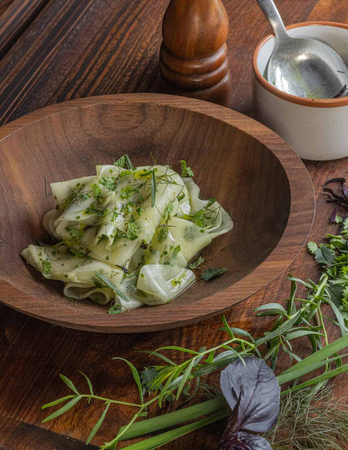 A finished shaved kohlrabi salad in a bowl tossed and garnished with herbs like burnet, opal basil, chives, tarragon, and herb infused oil.