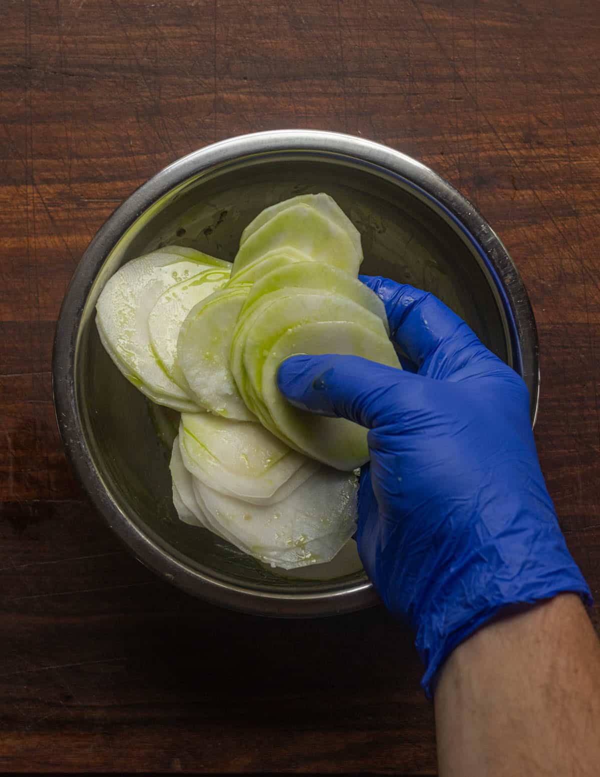 Mixing shaved kohlrabi with oil, lemon juice and salt in a bowl using gloves.