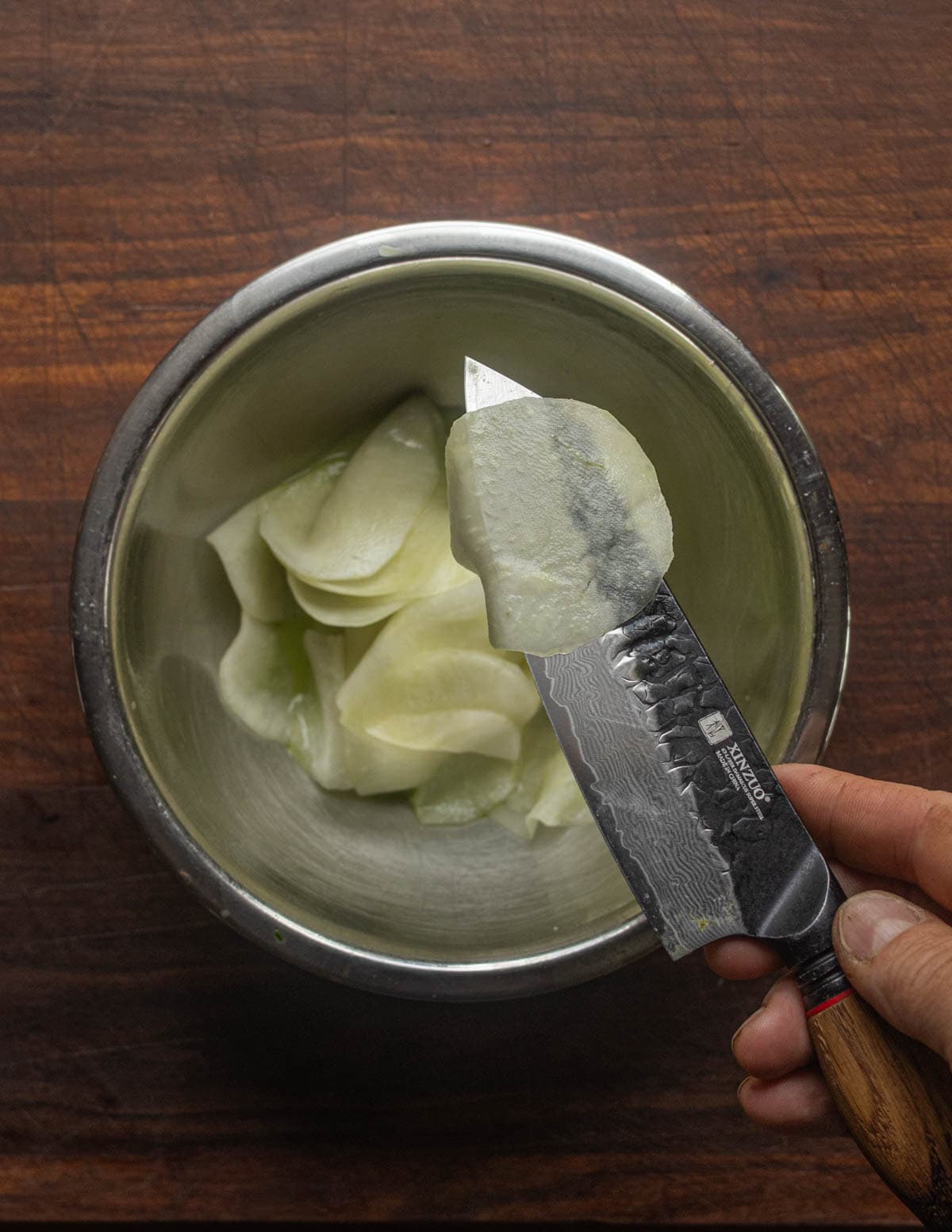 A knife holding up a slice of kohlrabi showing it's paper thin and translucent